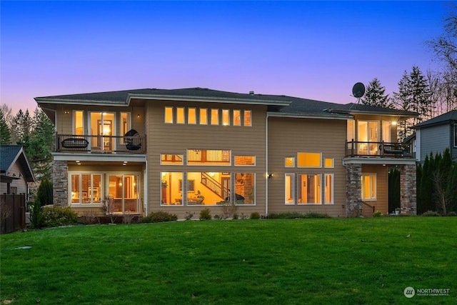 back house at dusk with a balcony and a yard