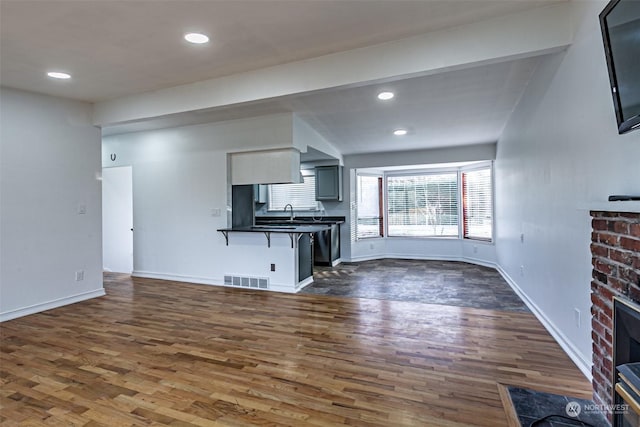 unfurnished living room with sink, lofted ceiling with beams, dark hardwood / wood-style floors, and a brick fireplace