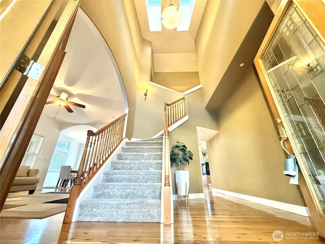 stairs featuring arched walkways, a towering ceiling, baseboards, and wood finished floors