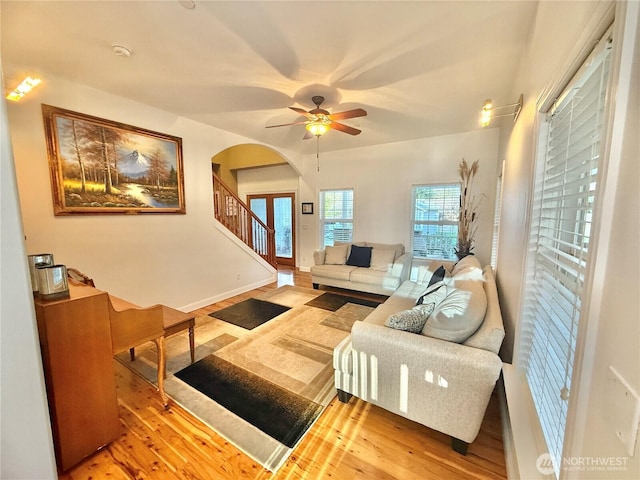 living room with arched walkways, stairway, wood finished floors, and a ceiling fan