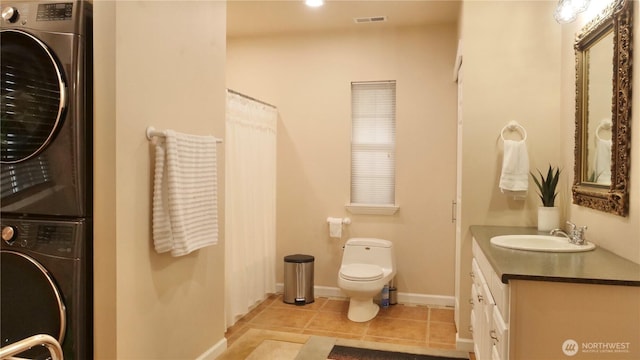 bathroom featuring toilet, stacked washer / dryer, vanity, tile patterned flooring, and baseboards