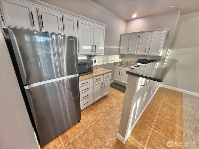 kitchen with light tile patterned floors, baseboards, freestanding refrigerator, a peninsula, and black microwave