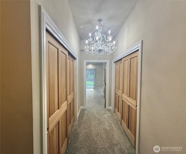 hallway with a chandelier, carpet floors, vaulted ceiling, and baseboards