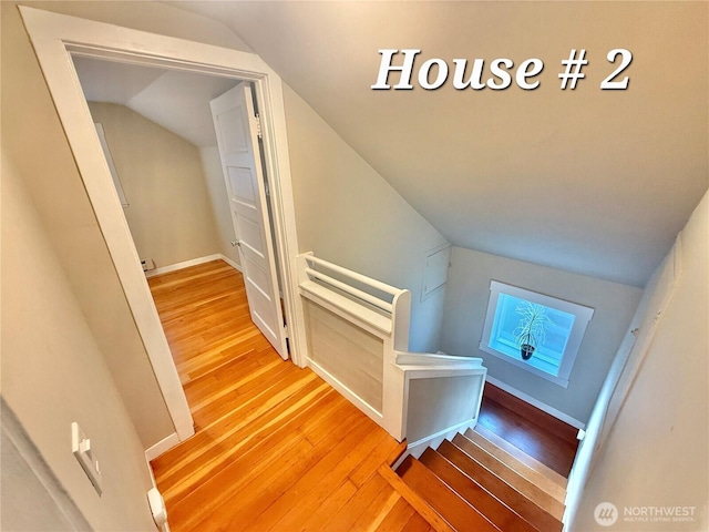 corridor with an upstairs landing, vaulted ceiling, baseboards, and wood finished floors