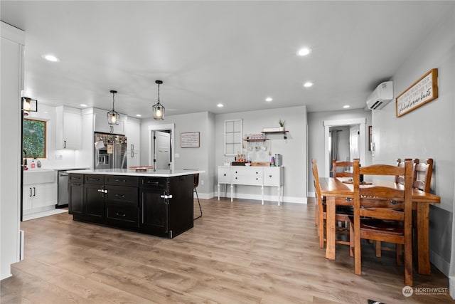 kitchen with appliances with stainless steel finishes, a kitchen island, white cabinetry, hanging light fixtures, and a wall unit AC