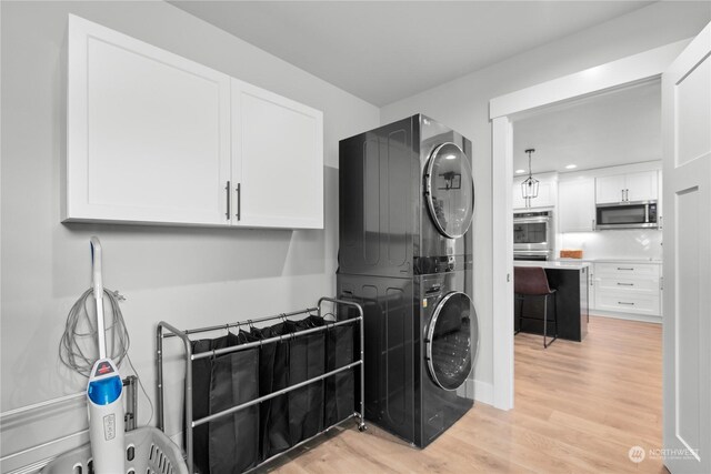 clothes washing area featuring light hardwood / wood-style floors, cabinets, and stacked washer and clothes dryer