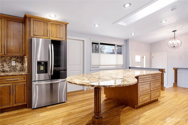 kitchen featuring stainless steel refrigerator with ice dispenser, hanging light fixtures, light stone countertops, a kitchen island, and decorative backsplash