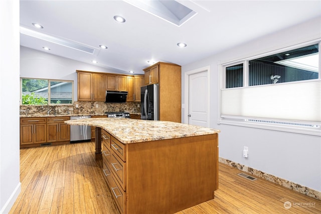 kitchen featuring vaulted ceiling, appliances with stainless steel finishes, light stone counters, a center island, and light hardwood / wood-style floors