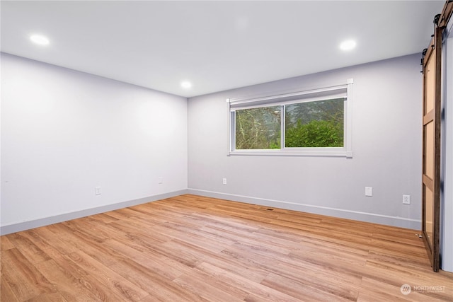 empty room with light hardwood / wood-style floors and a barn door