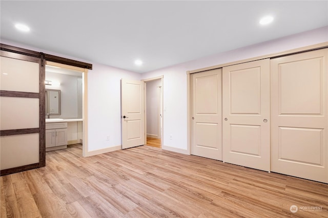 unfurnished bedroom featuring ensuite bathroom, a barn door, a closet, sink, and light hardwood / wood-style flooring