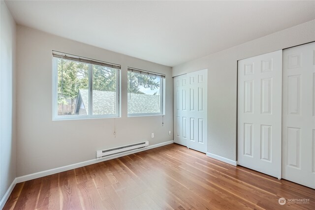 unfurnished bedroom with light wood-type flooring, a baseboard heating unit, and two closets