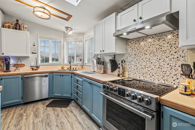 kitchen with appliances with stainless steel finishes, sink, white cabinets, and wall chimney exhaust hood