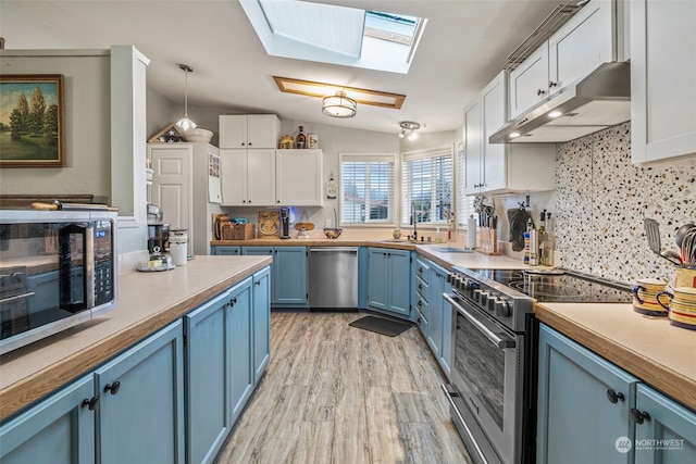 kitchen featuring blue cabinetry, white cabinetry, appliances with stainless steel finishes, pendant lighting, and vaulted ceiling with skylight