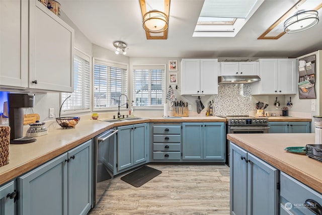 kitchen featuring a skylight, blue cabinets, white cabinetry, sink, and stainless steel appliances