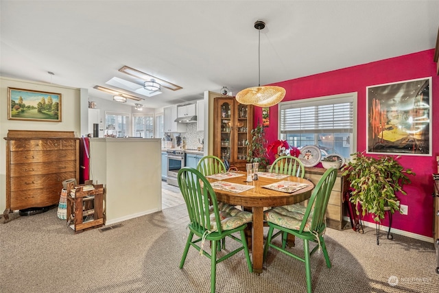 dining area featuring light colored carpet and lofted ceiling with skylight