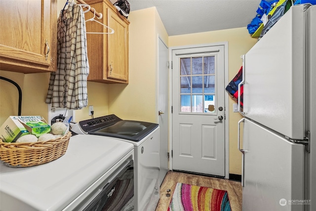 laundry room featuring cabinets, washer and clothes dryer, a textured ceiling, and light hardwood / wood-style floors