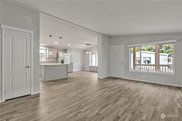 unfurnished living room featuring light wood-type flooring, a wealth of natural light, an inviting chandelier, and lofted ceiling