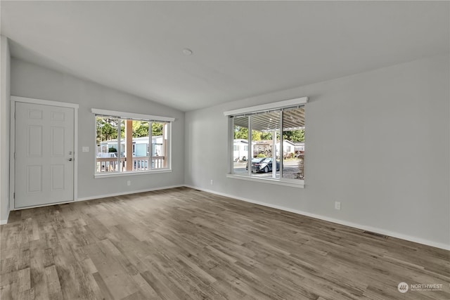 unfurnished room with light wood-type flooring, vaulted ceiling, and plenty of natural light