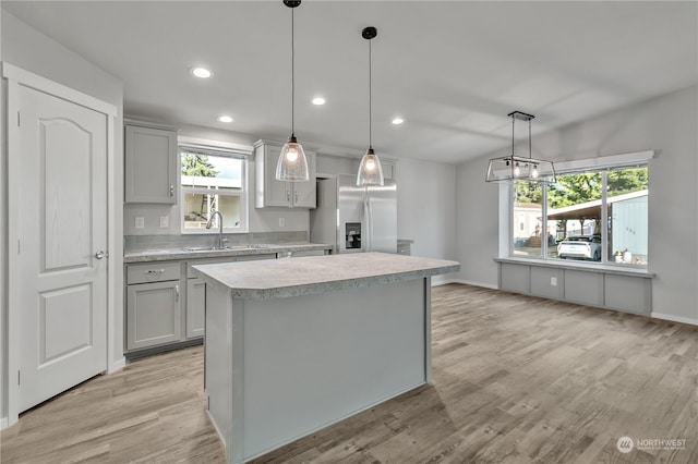 kitchen featuring stainless steel fridge with ice dispenser, decorative light fixtures, a kitchen island, and gray cabinetry