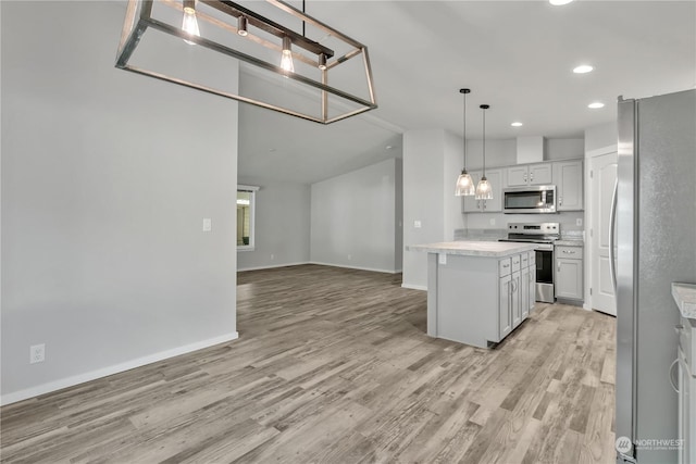 kitchen with stainless steel appliances, a kitchen island, hanging light fixtures, and light hardwood / wood-style flooring