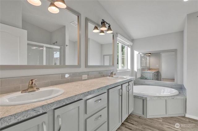 bathroom featuring independent shower and bath, vaulted ceiling, wood-type flooring, vanity, and backsplash