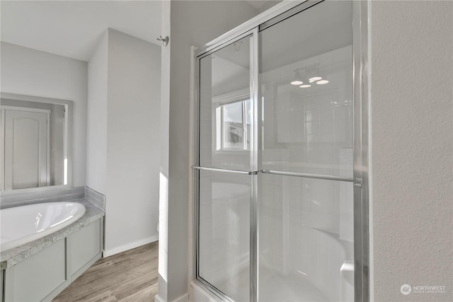 bathroom with wood-type flooring and shower with separate bathtub