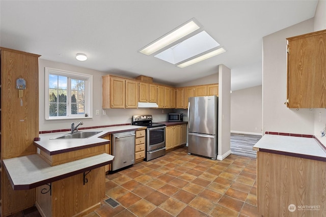 kitchen featuring sink, a breakfast bar area, lofted ceiling with skylight, stainless steel appliances, and kitchen peninsula