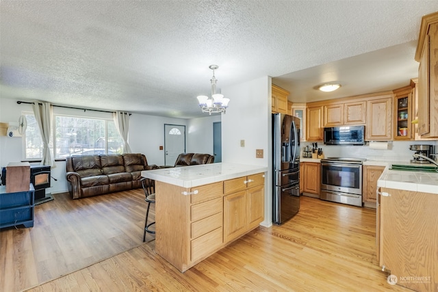 kitchen with sink, hanging light fixtures, stainless steel appliances, kitchen peninsula, and light wood-type flooring