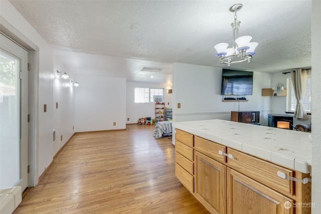 kitchen featuring tile countertops, a notable chandelier, a textured ceiling, and light hardwood / wood-style flooring