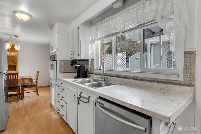 kitchen featuring sink, light wood-type flooring, stainless steel dishwasher, white cabinets, and backsplash