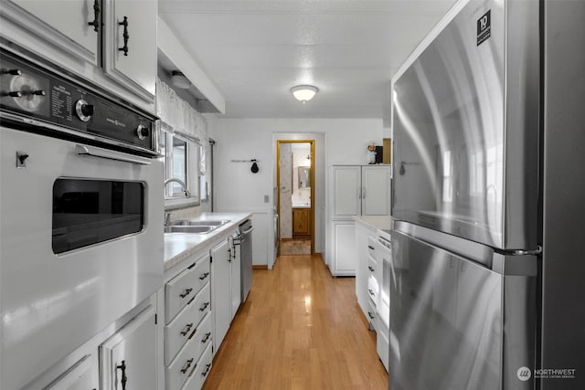 kitchen featuring sink, light wood-type flooring, white cabinetry, and appliances with stainless steel finishes