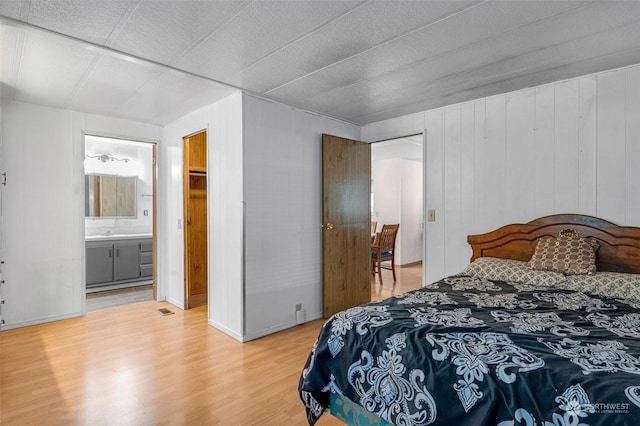 bedroom with sink, hardwood / wood-style floors, ensuite bath, and wooden walls