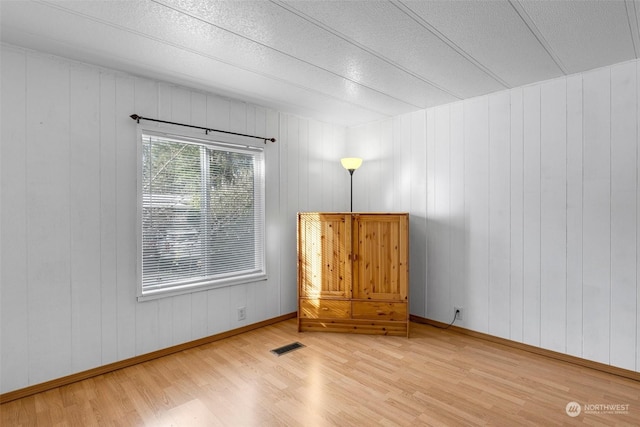 unfurnished room featuring hardwood / wood-style floors, wooden walls, and a textured ceiling