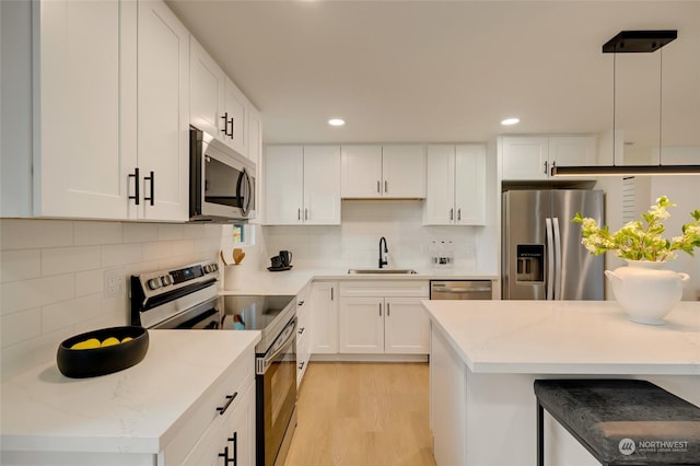 kitchen featuring appliances with stainless steel finishes, hanging light fixtures, sink, light wood-type flooring, and white cabinets