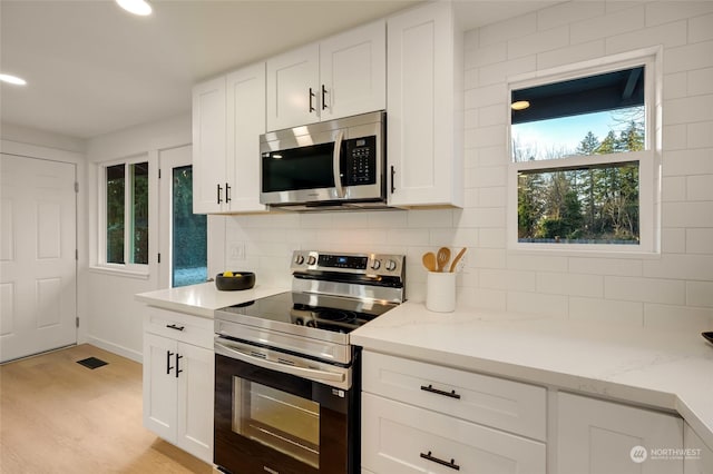 kitchen featuring light stone counters, backsplash, white cabinetry, and stainless steel appliances