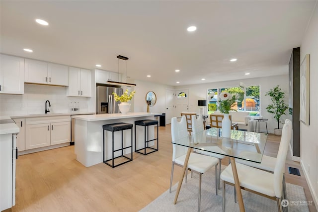 kitchen featuring stainless steel refrigerator with ice dispenser, decorative light fixtures, sink, white cabinetry, and a kitchen island