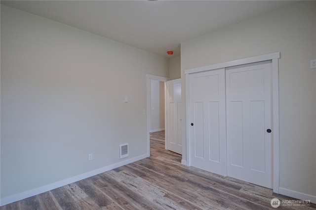 unfurnished bedroom featuring light wood finished floors, baseboards, visible vents, and a closet