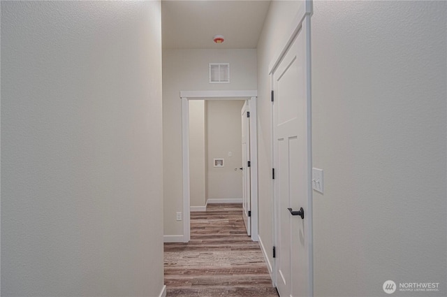 corridor with light wood-type flooring, visible vents, and baseboards