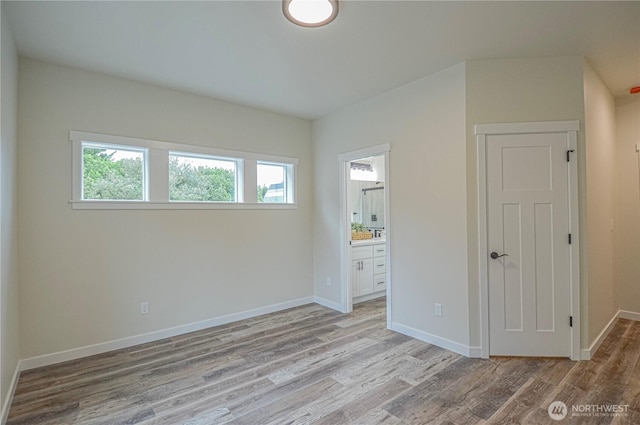 unfurnished bedroom featuring light wood-type flooring, baseboards, and connected bathroom