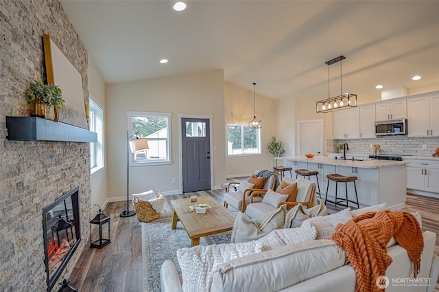 living area with recessed lighting, a large fireplace, wood finished floors, high vaulted ceiling, and baseboards