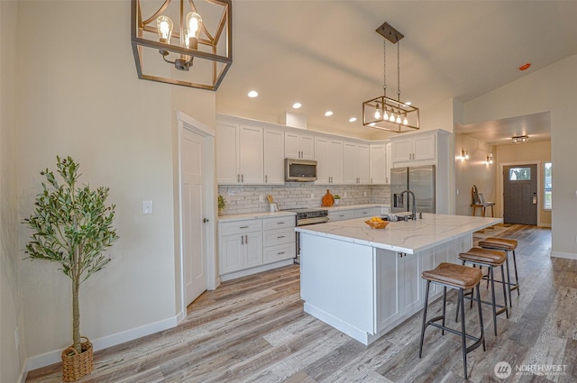 kitchen with appliances with stainless steel finishes, an island with sink, a breakfast bar area, and white cabinetry