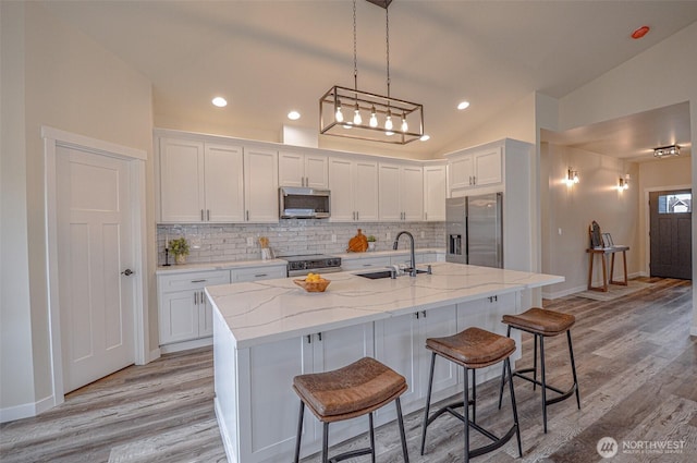 kitchen with stainless steel appliances, white cabinetry, a sink, and a center island with sink