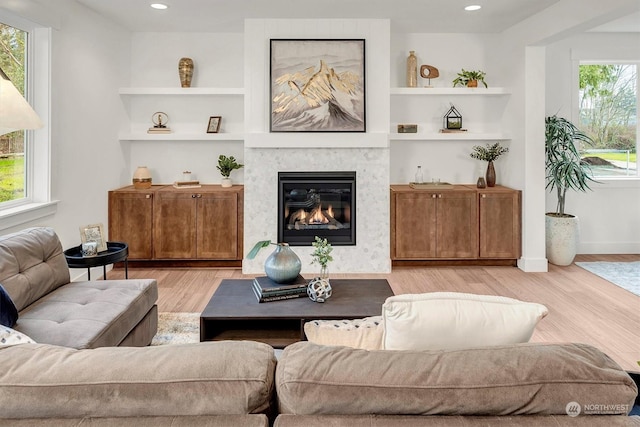 living area with baseboards, a glass covered fireplace, light wood-style floors, built in shelves, and recessed lighting