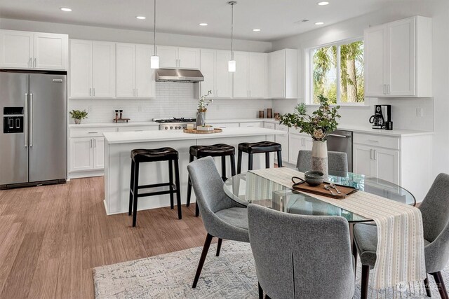 kitchen featuring stainless steel appliances, ventilation hood, light wood-type flooring, and light countertops