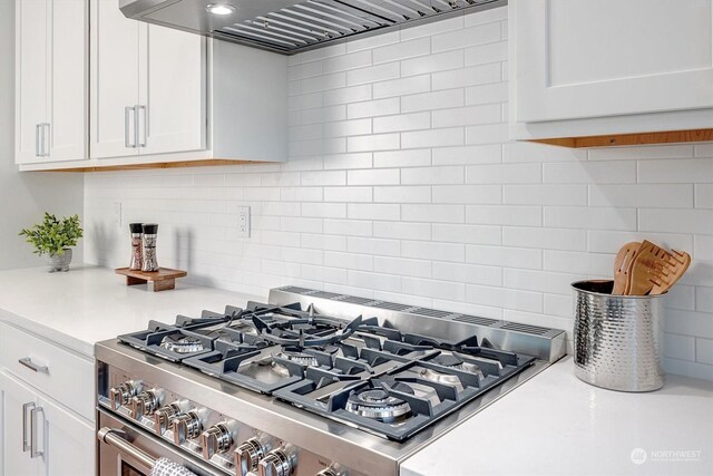 kitchen featuring light countertops, decorative backsplash, white cabinets, stainless steel gas range, and premium range hood