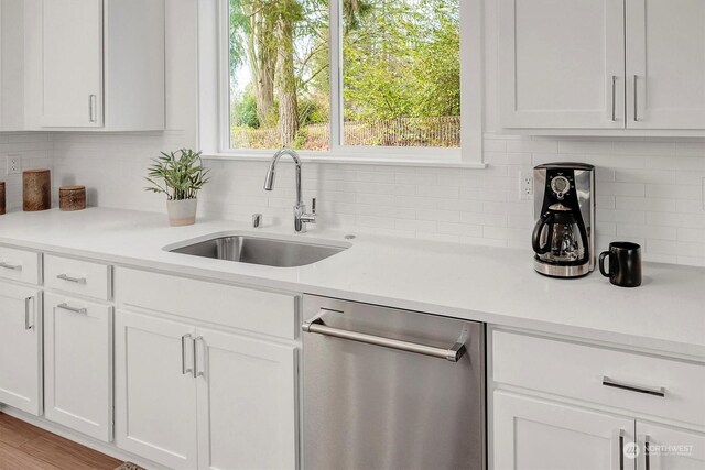 kitchen with tasteful backsplash, light countertops, white cabinetry, a sink, and dishwasher