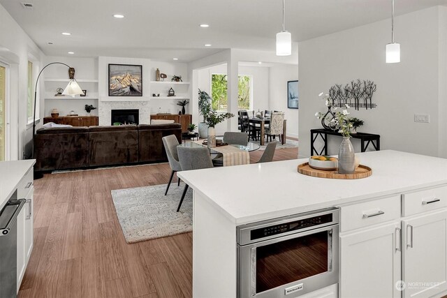 kitchen with a fireplace, light countertops, hanging light fixtures, light wood-style flooring, and white cabinets