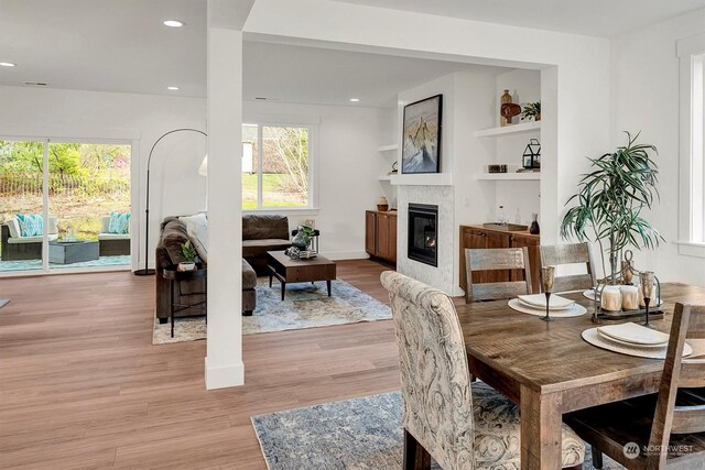 dining room with built in features, light wood finished floors, recessed lighting, a glass covered fireplace, and baseboards