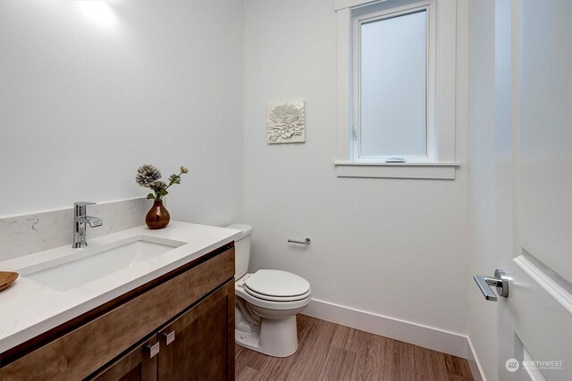 half bathroom featuring wood finished floors, vanity, toilet, and baseboards