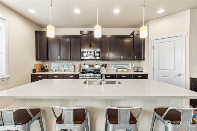 kitchen with a kitchen bar, pendant lighting, appliances with stainless steel finishes, and a center island with sink